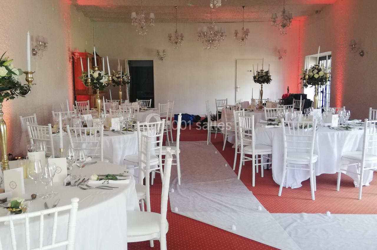 Salle de réception décorée avec des tables rondes, chaises blanches et centres de table fleuris.