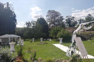 Jardin ensoleillé aménagé pour un événement avec tables hautes, tente blanche et allée décorée de fleurs.