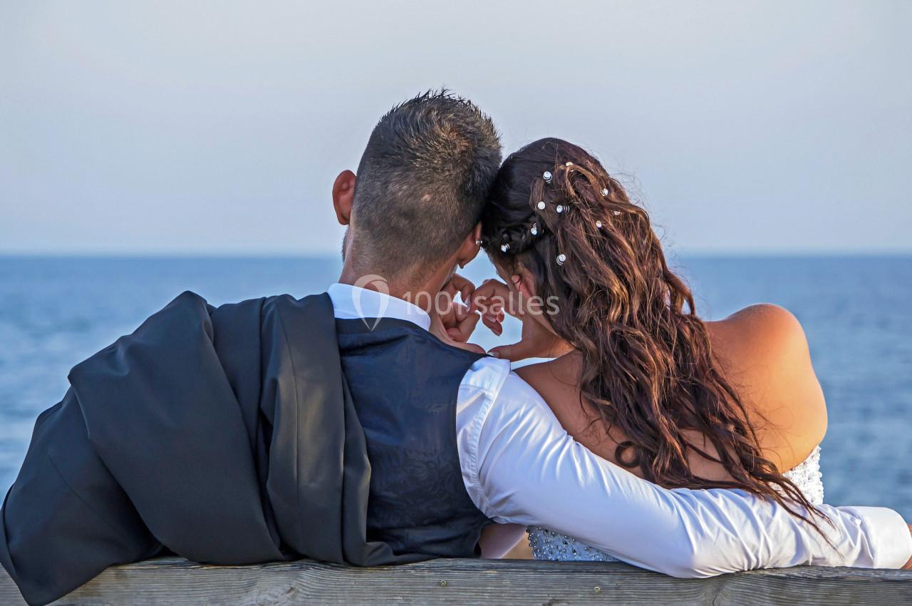 Un couple assis sur un banc en bois, regardant la mer au coucher du soleil.