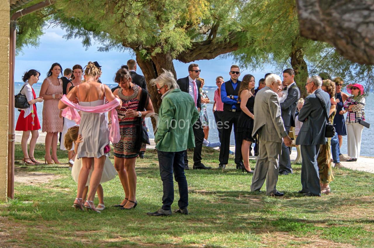 Groupe de personnes en tenue élégante discutant en extérieur près d'un arbre et d'une étendue d'eau.