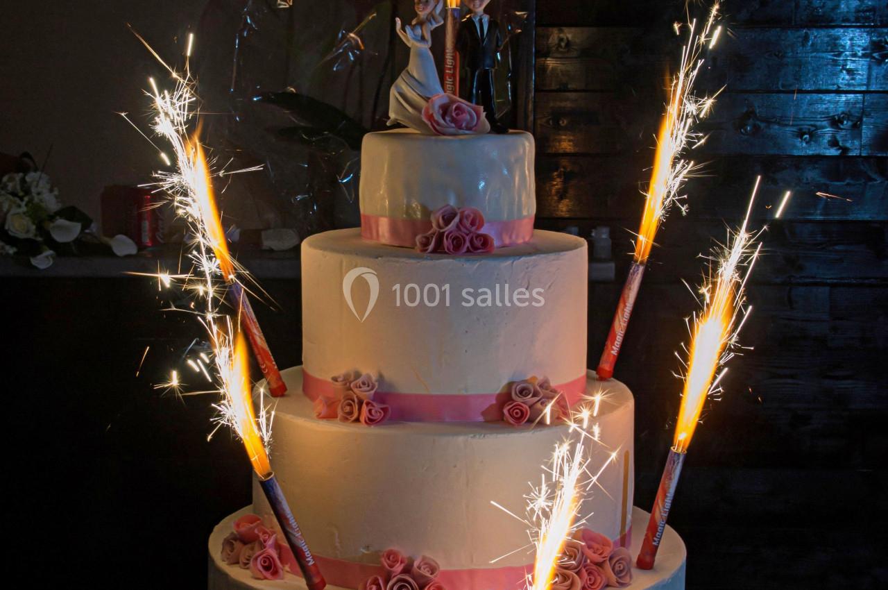 Gâteau de mariage à quatre étages décoré de roses roses et de cierges magiques allumés.