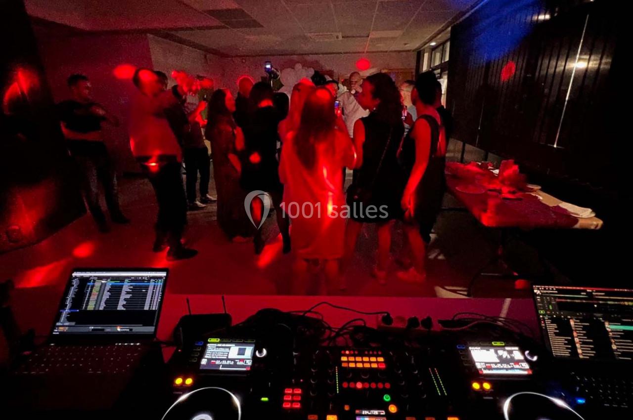 Vue d'une piste de danse animée avec des lumières rouges, des invités et une table de mixage au premier plan.