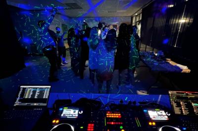 Vue depuis une table de mixage sur un groupe de personnes dansant dans une salle éclairée par une lumière rouge.