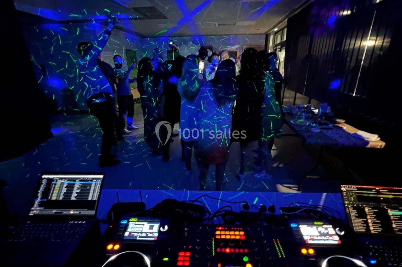 Des personnes dansent sous des lumières colorées dans une salle sombre, vue depuis une table de mixage avec équipements DJ.