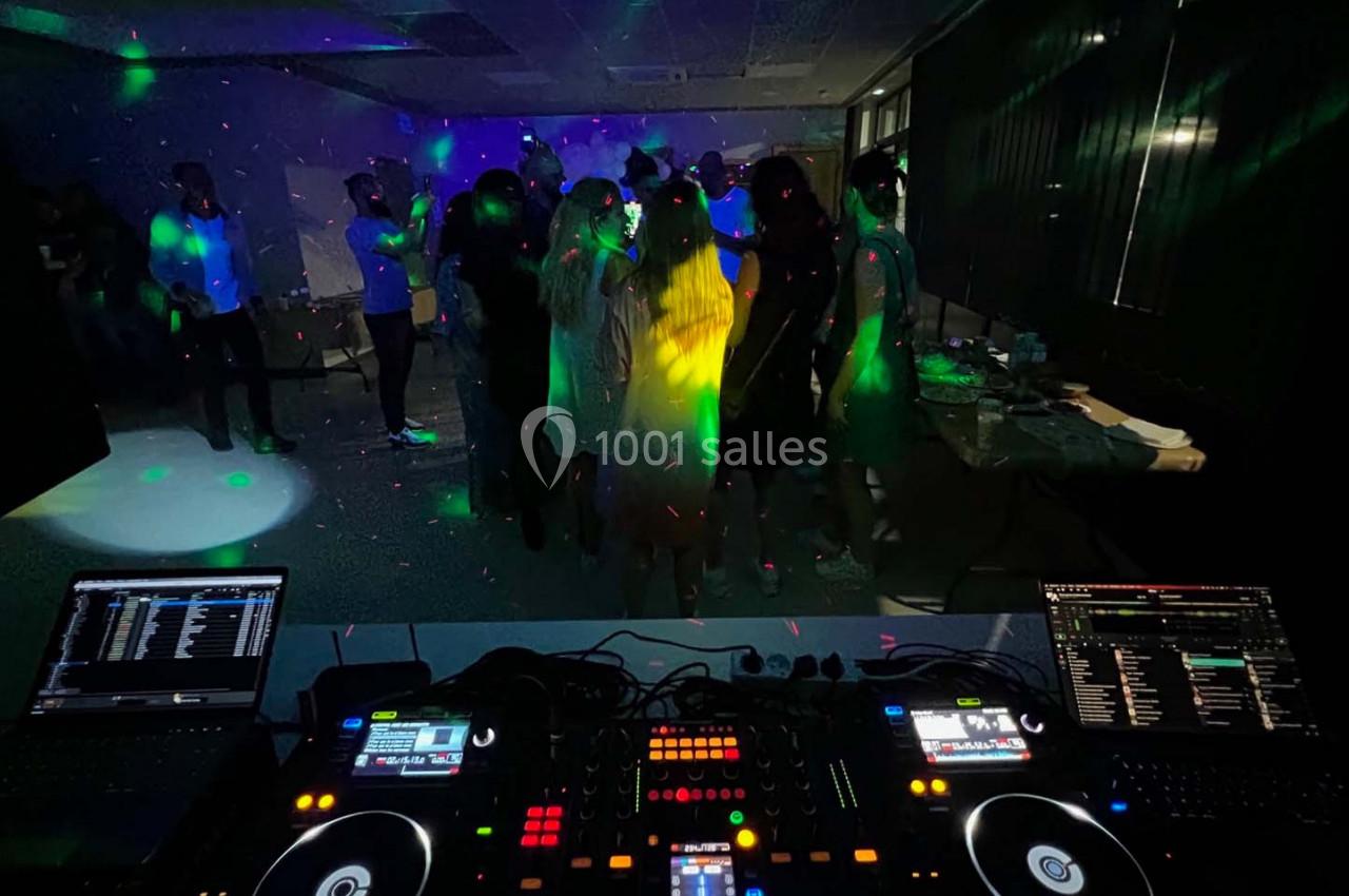 Vue depuis une table de mixage sur une piste de danse éclairée par des lumières colorées dans une salle sombre.