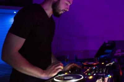 Vue depuis une table de mixage sur un groupe de personnes dansant dans une salle éclairée par une lumière rouge.