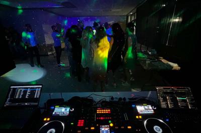 Vue depuis une table de mixage sur un groupe de personnes dansant dans une salle éclairée par une lumière rouge.