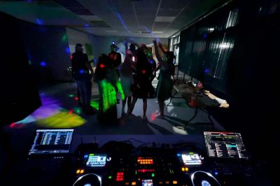 Vue depuis une table de mixage sur un groupe de personnes dansant dans une salle éclairée par une lumière rouge.