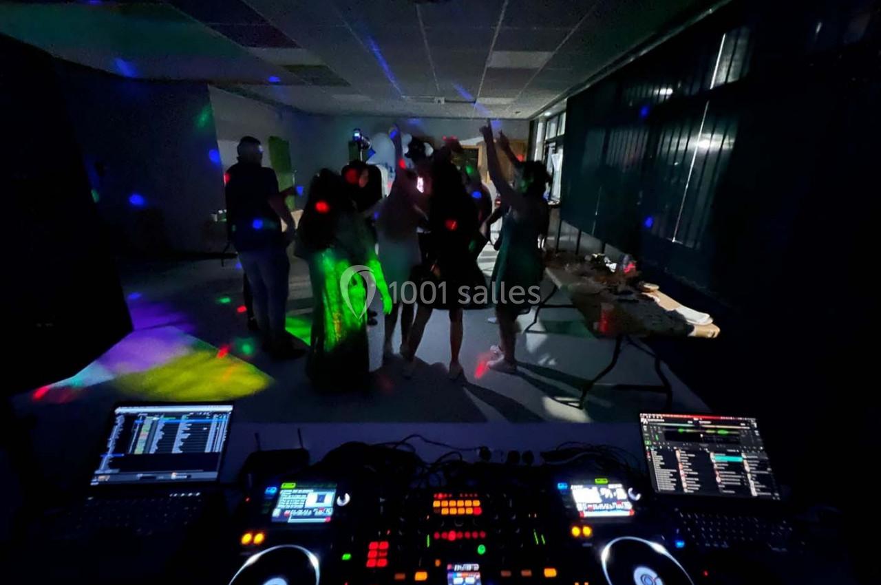 Personnes dansant sous des lumières colorées dans une salle sombre, avec une table de mixage en premier plan.