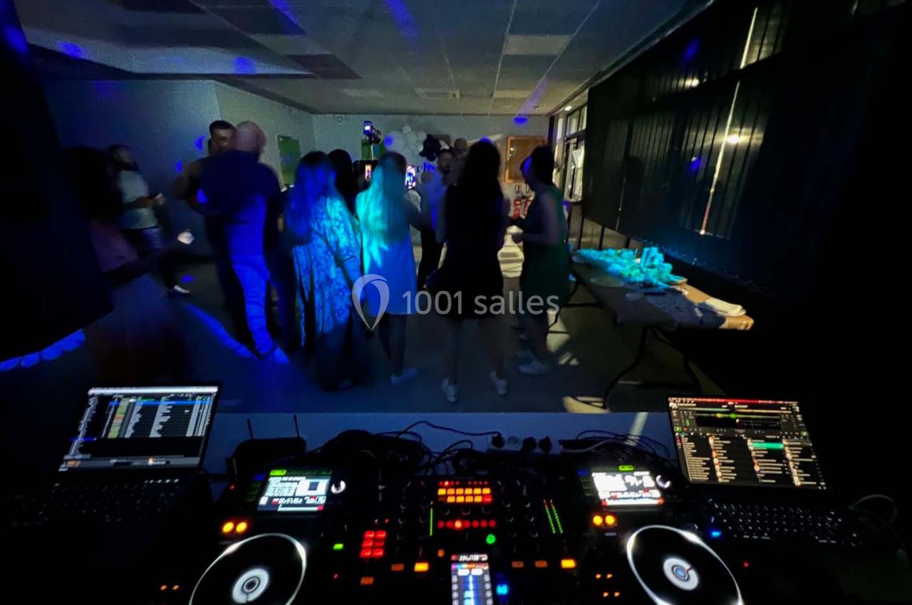 Vue depuis une table de mixage DJ avec des invités dansant dans une salle faiblement éclairée.