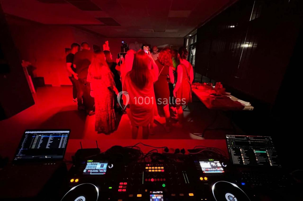 Vue depuis une table de mixage sur un groupe de personnes dansant dans une salle éclairée par une lumière rouge.