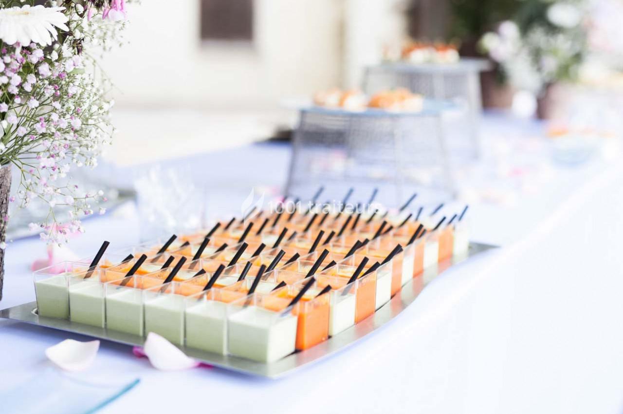 Plateau de verrines colorées alignées, contenant des préparations vertes et orange, sur une table de réception.