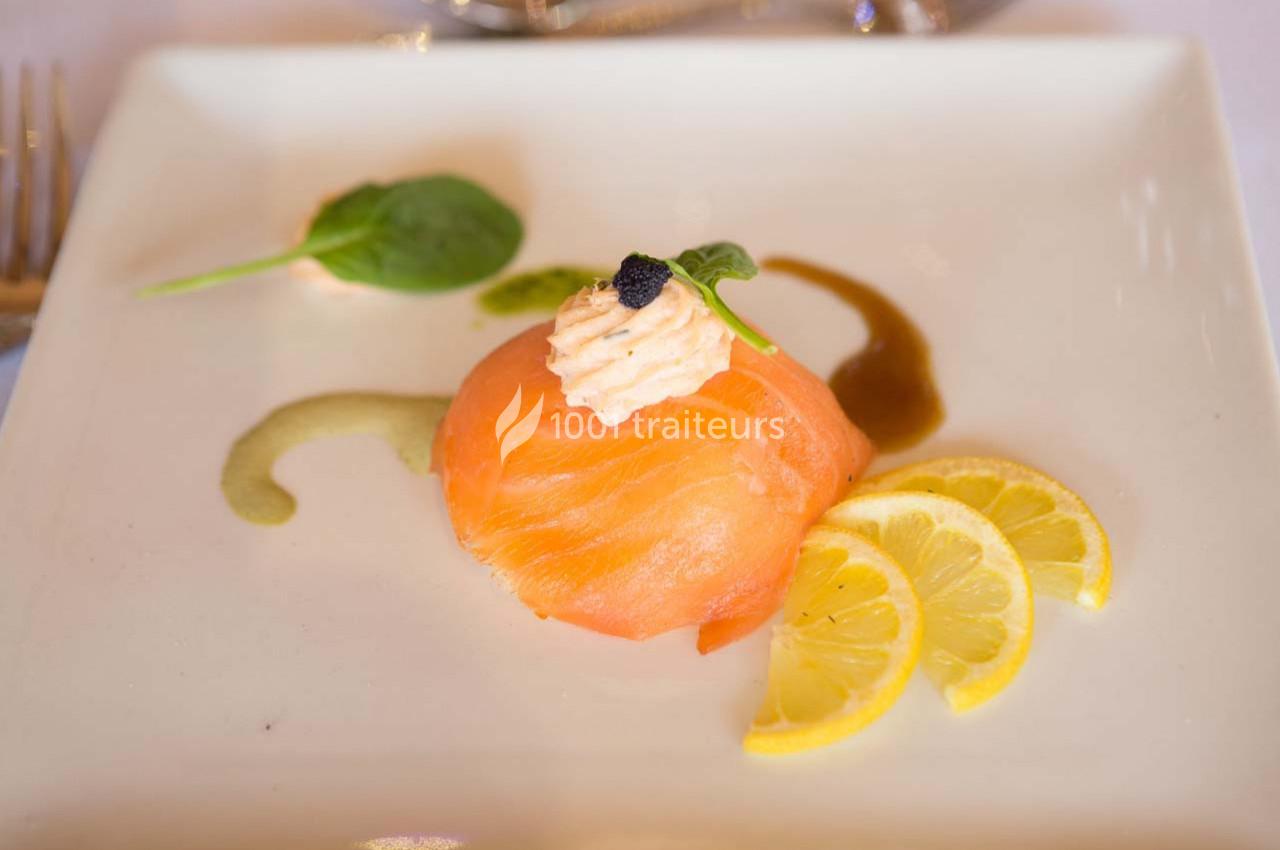 Tranche de saumon fumé garnie de crème et caviar, accompagnée de rondelles de citron et d'épinard sur une assiette blanche.