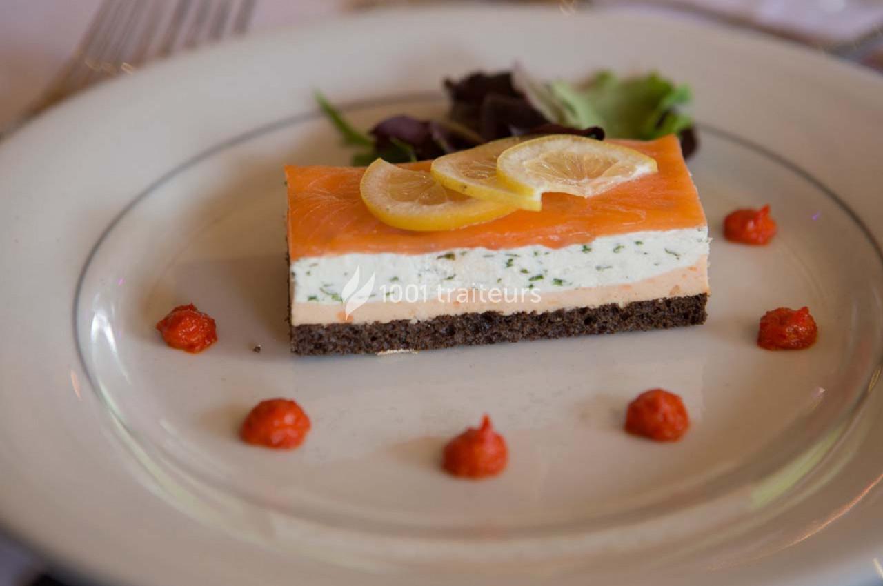 Entrée composée de saumon fumé, mousse aux herbes, pain noir, tranches de citron et décor de sauce rouge.