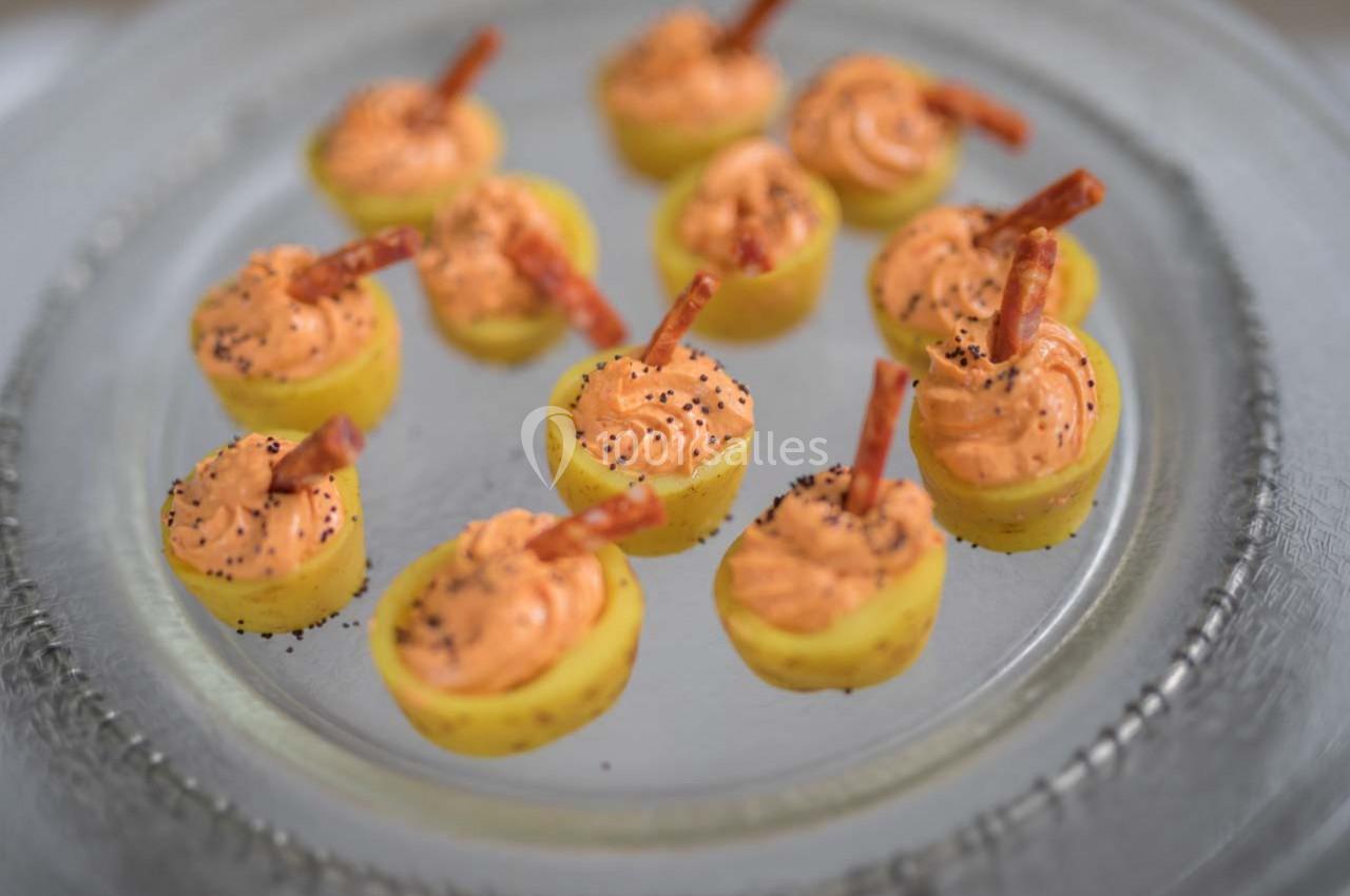 Pommes de terre miniatures garnies de mousse orange, décorées de bâtonnets et de graines noires, sur une assiette en verre.