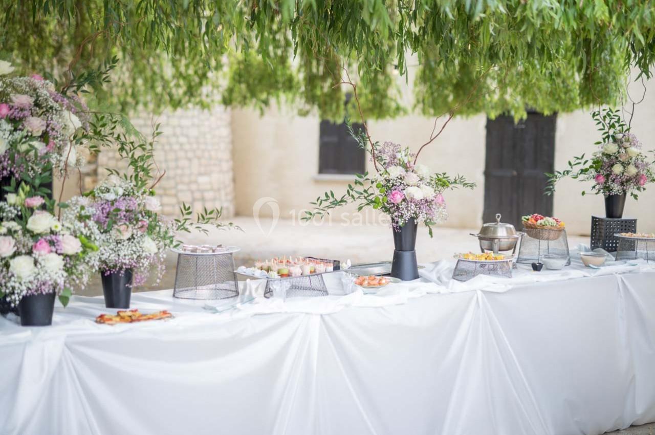 Table de buffet décorée de fleurs et plats variés, installée en extérieur sous des branches tombantes.