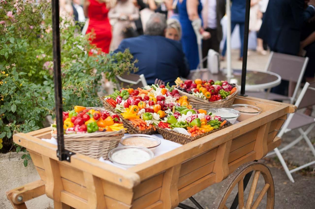 Chariot en bois contenant des paniers de légumes colorés et des sauces, disposé dans un cadre extérieur lors d'un événement.