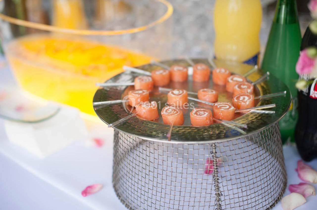 Plateau de roulés de saumon disposés en cercle sur une grille métallique, entouré de boissons et décorations.