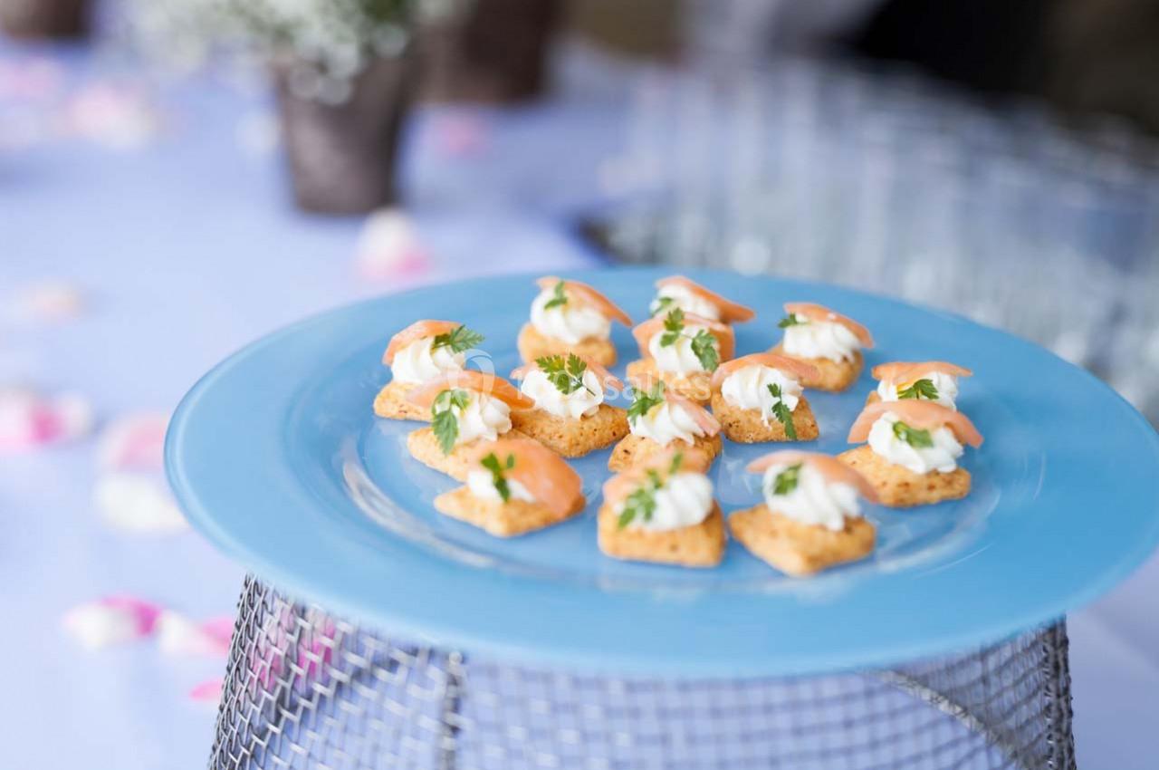 Assortiment de canapés au saumon et crème disposés sur une assiette bleue, avec un fond flou de table décorée.