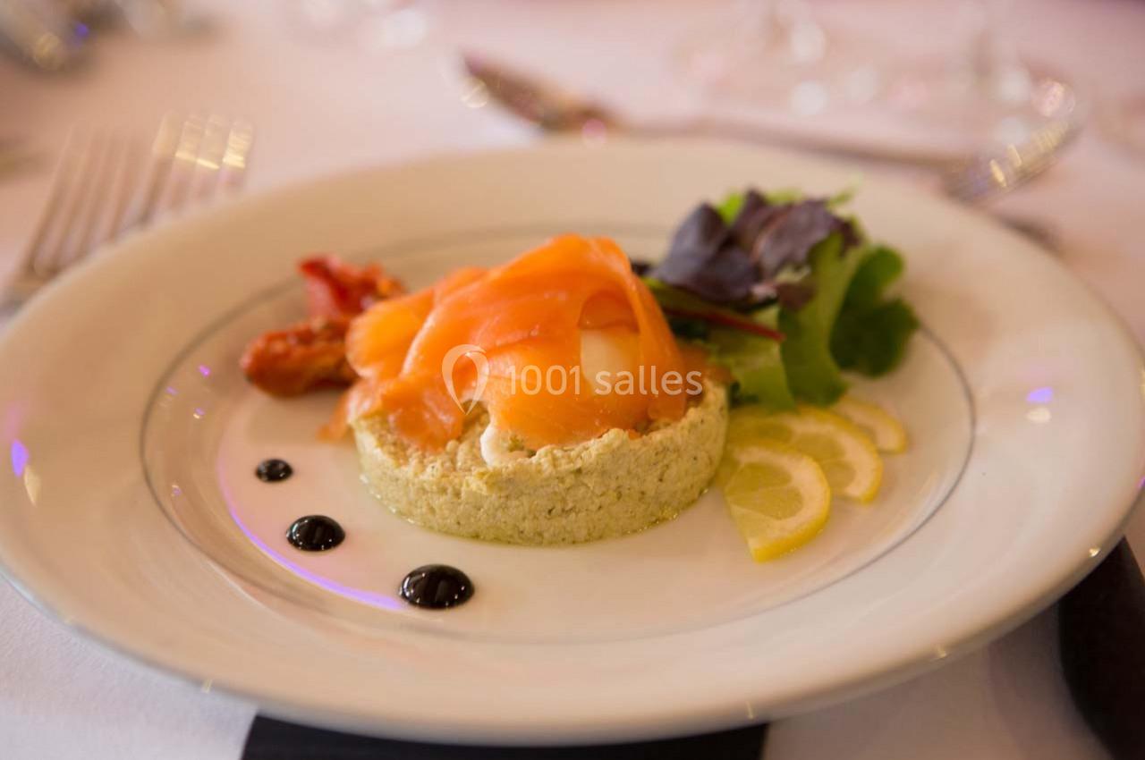 Assiette avec une tartelette garnie de saumon fumé, accompagnée de salade, rondelles de citron et sauce balsamique.