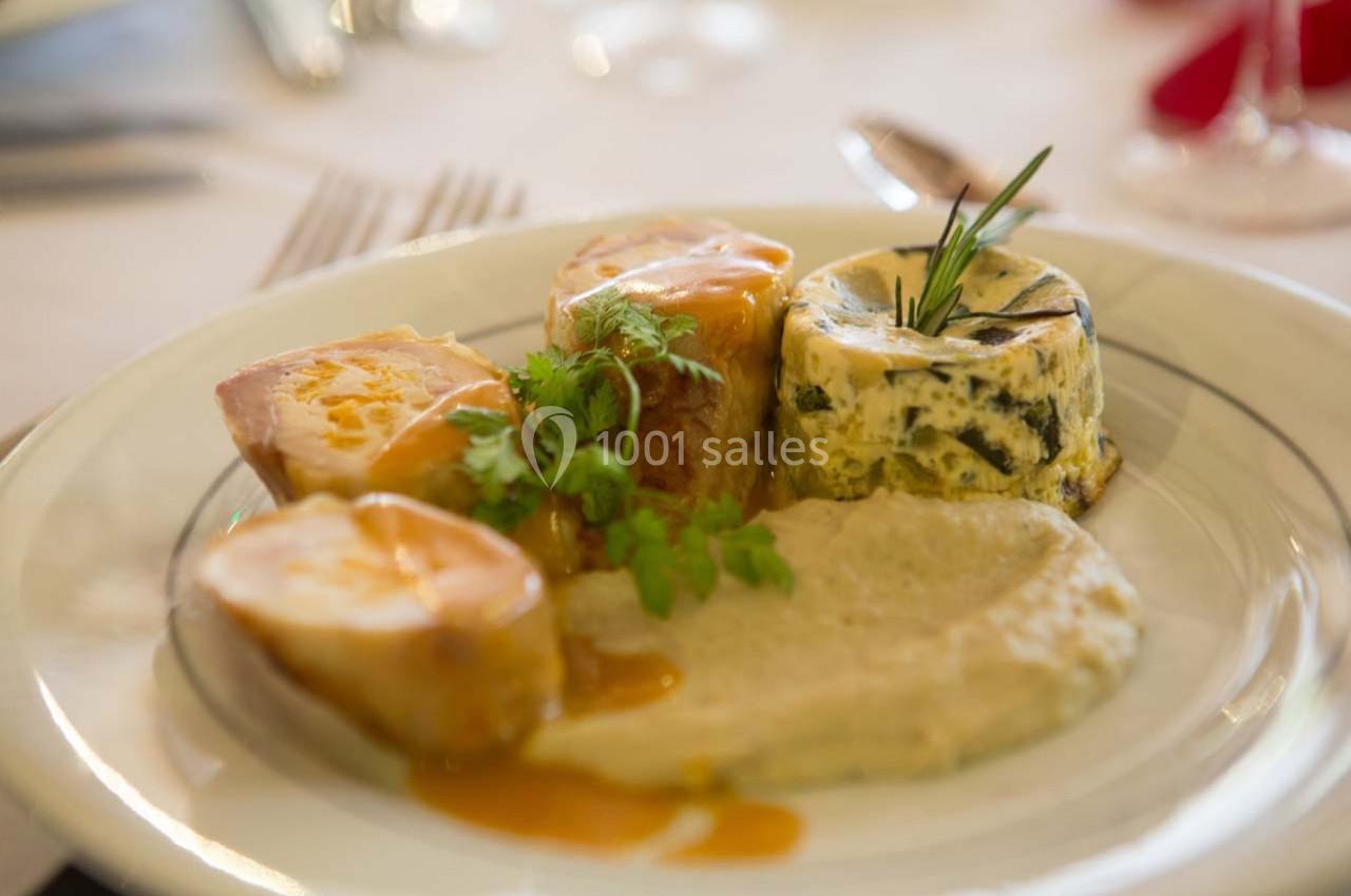 Assiette contenant des médaillons de viande, une purée, un flan aux légumes et une sauce, servie sur une table dressée.