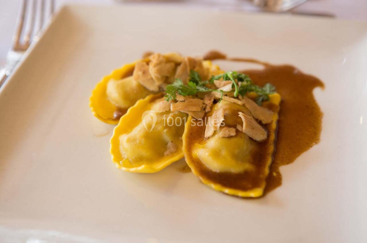 Assiette de raviolis garnis, nappés de sauce brune et garnis de morceaux de viande et de persil.