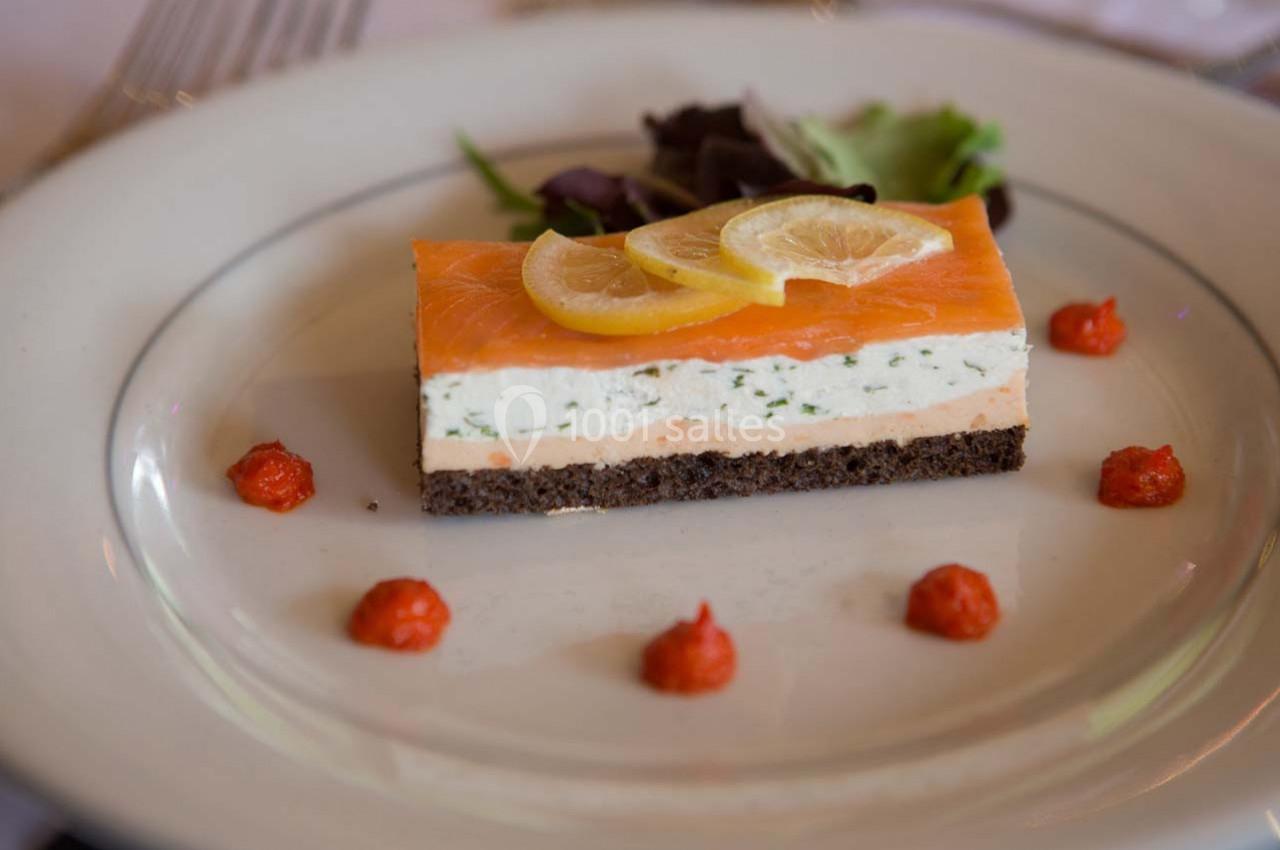 Entrée composée de saumon fumé, mousse aux herbes, pain noir, rondelles de citron et décorée de salade et sauce rouge.