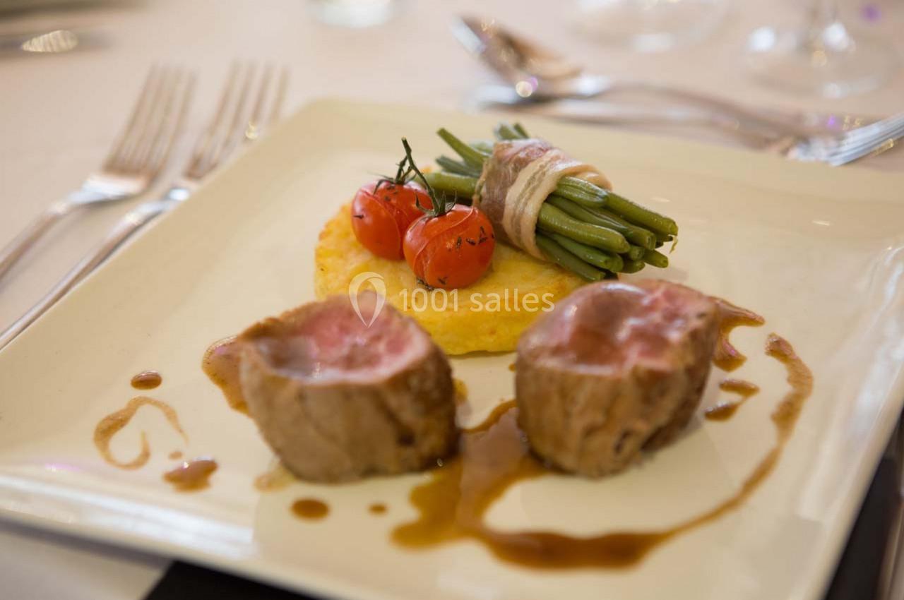 Assiette gastronomique avec deux morceaux de viande, haricots verts enroulés de lard, tomates cerises et sauce.