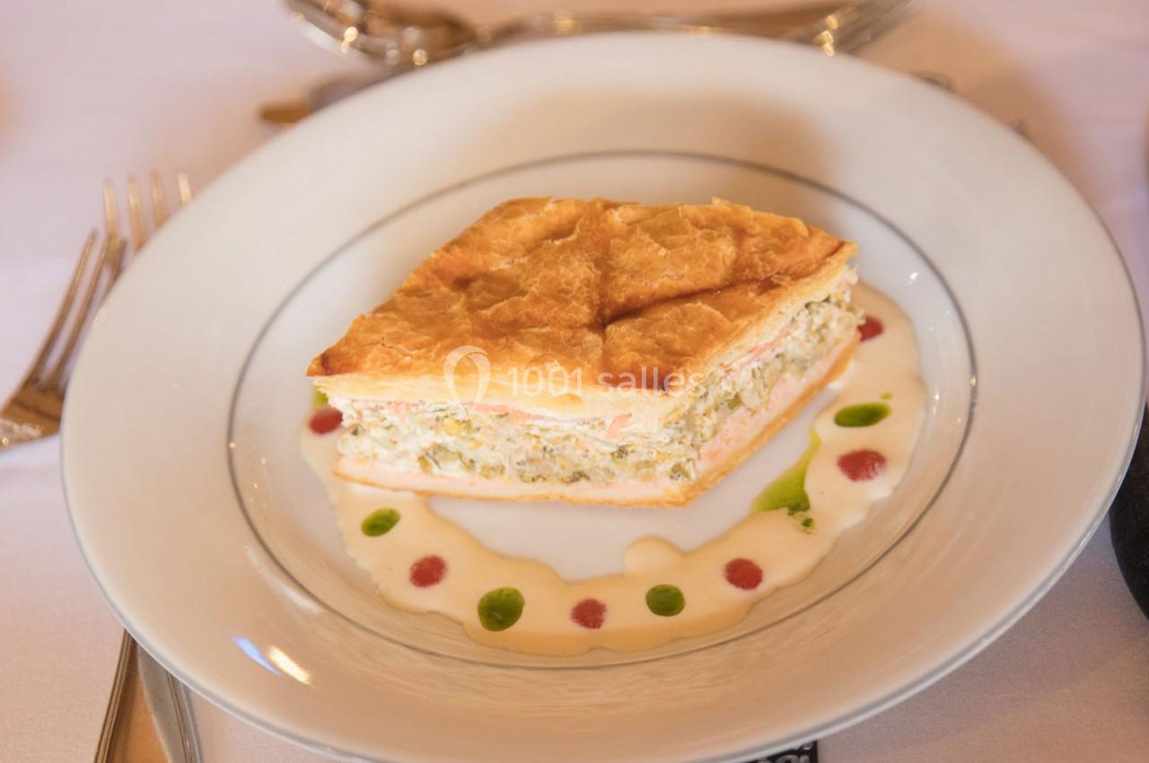 Part de feuilleté garni, servie sur une assiette avec une sauce décorative et des couverts en arrière-plan.