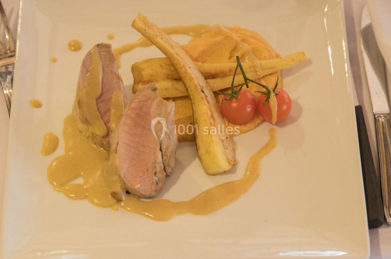 Assiette de viande tranchée avec sauce, purée, panais rôtis et tomates cerises sur une table dressée.