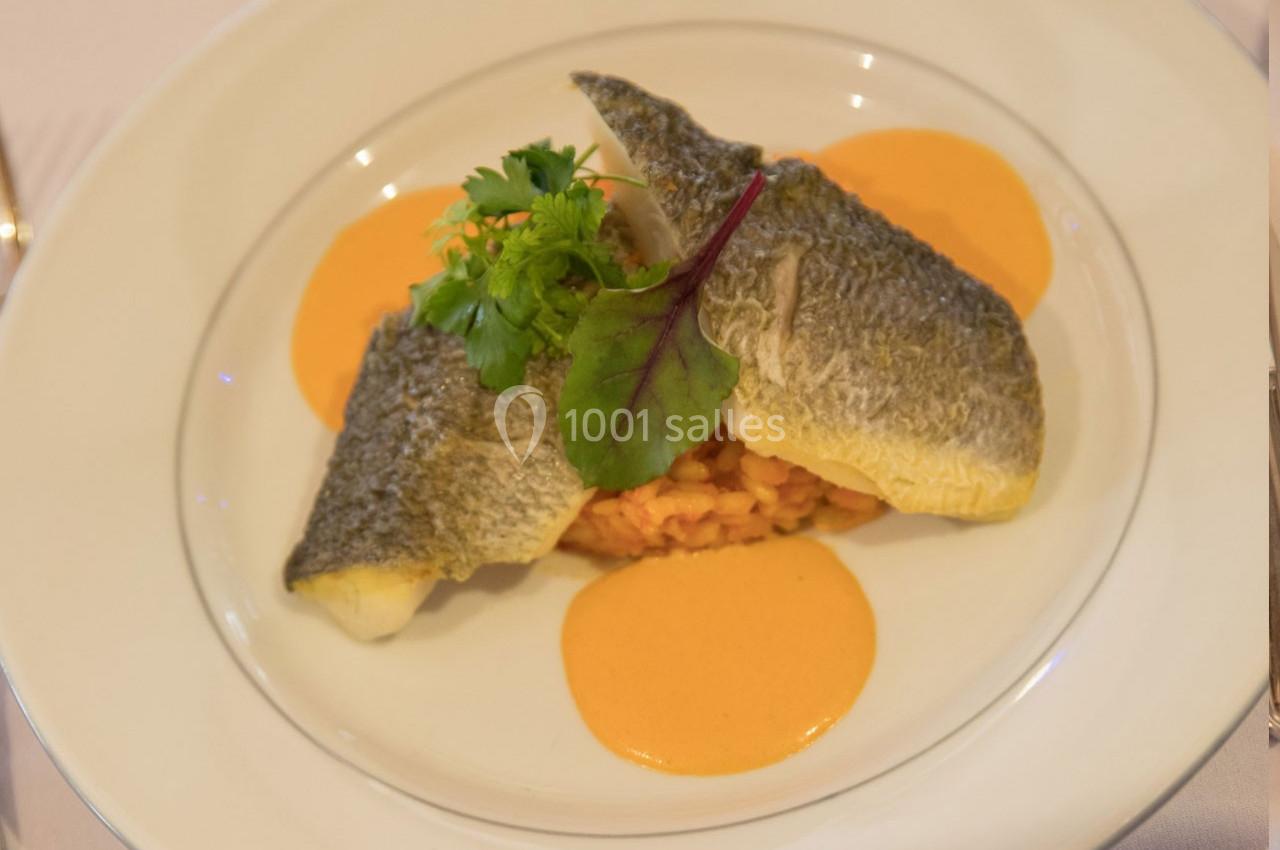 Filets de poisson servis sur un lit de risotto, accompagnés de sauce orange et décorés de feuilles de salade.