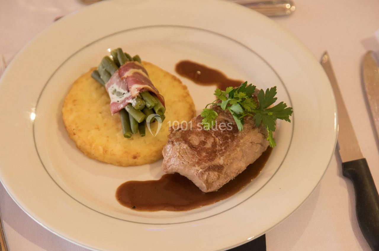 Assiette contenant un filet de viande avec sauce, haricots verts enroulés de lard et galette de pommes de terre.
