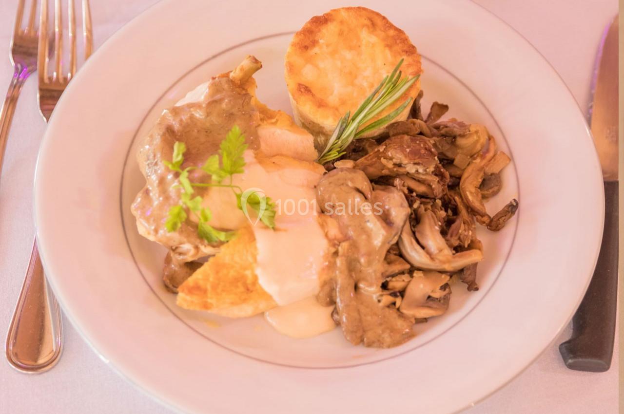 Assiette contenant du poulet en sauce, champignons sautés, gratin et garniture de romarin, servie sur une table dressée.