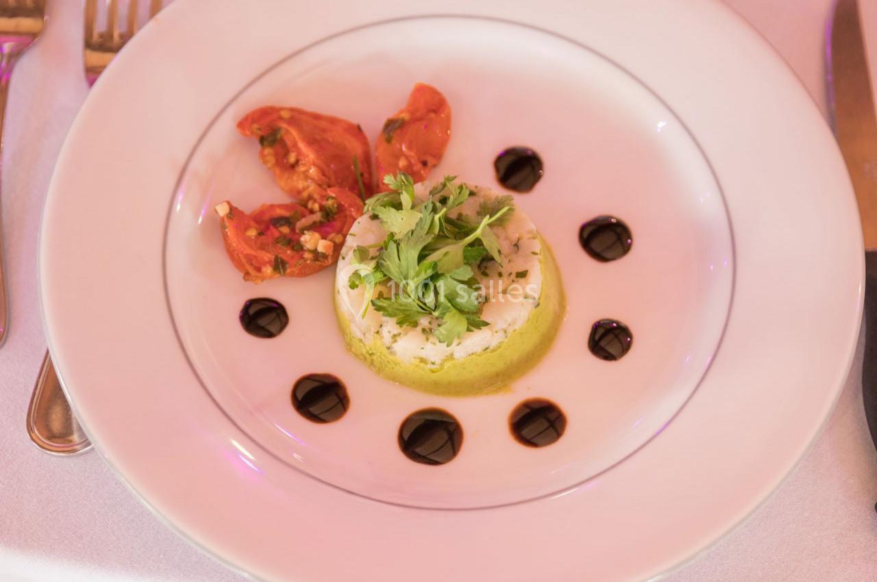 Assiette contenant une mousse verte garnie d'herbes, accompagnée de tomates rôties et de points de sauce balsamique.