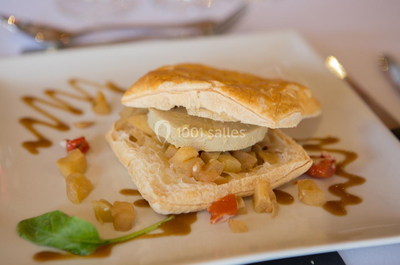 Feuilleté garni de foie gras et pommes caramélisées, accompagné de sauce décorative et de légumes sur une assiette blanche.