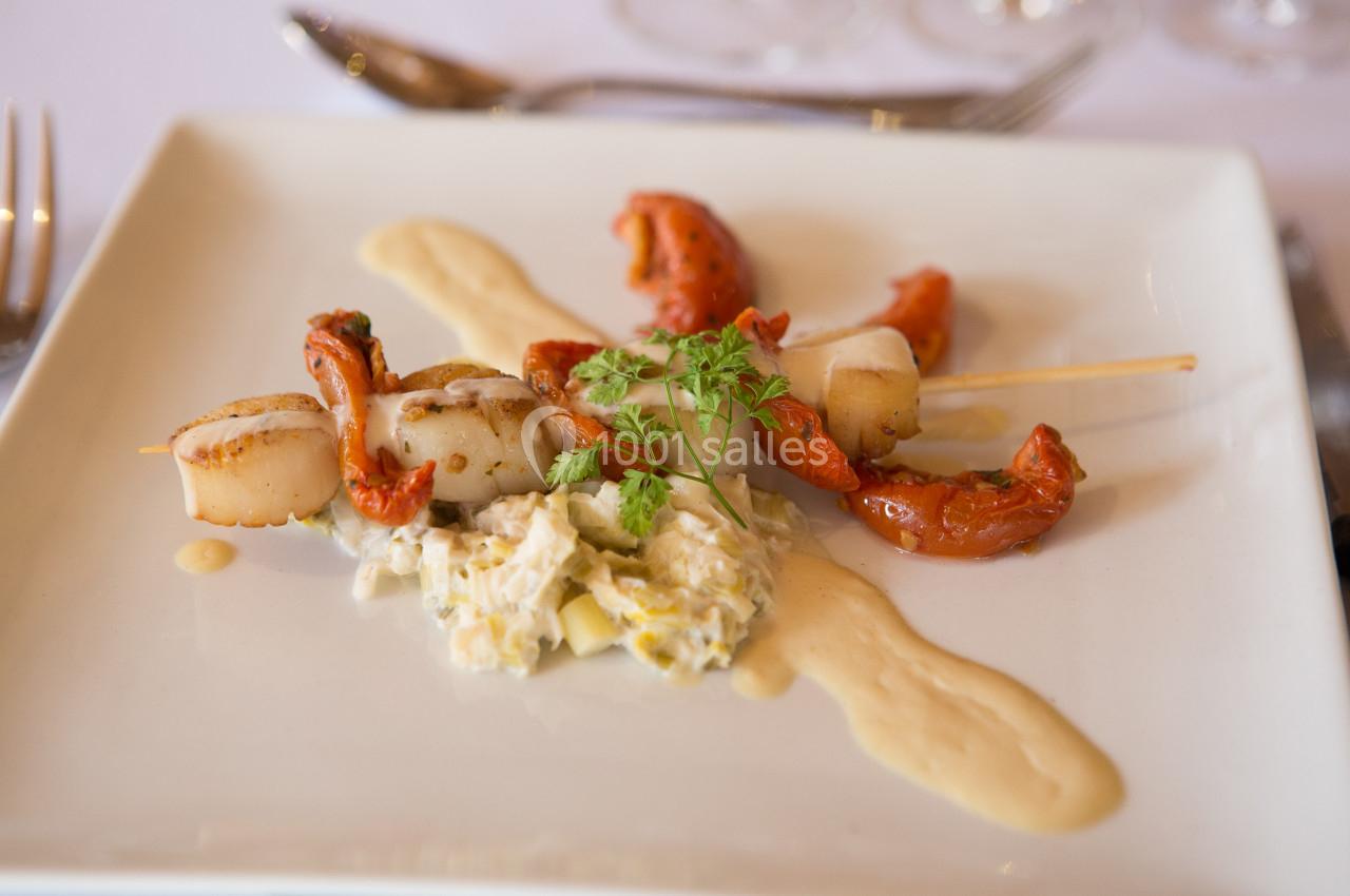 Brochette de noix de Saint-Jacques avec tomates confites, purée et salade crémeuse, présentée sur une assiette blanche.