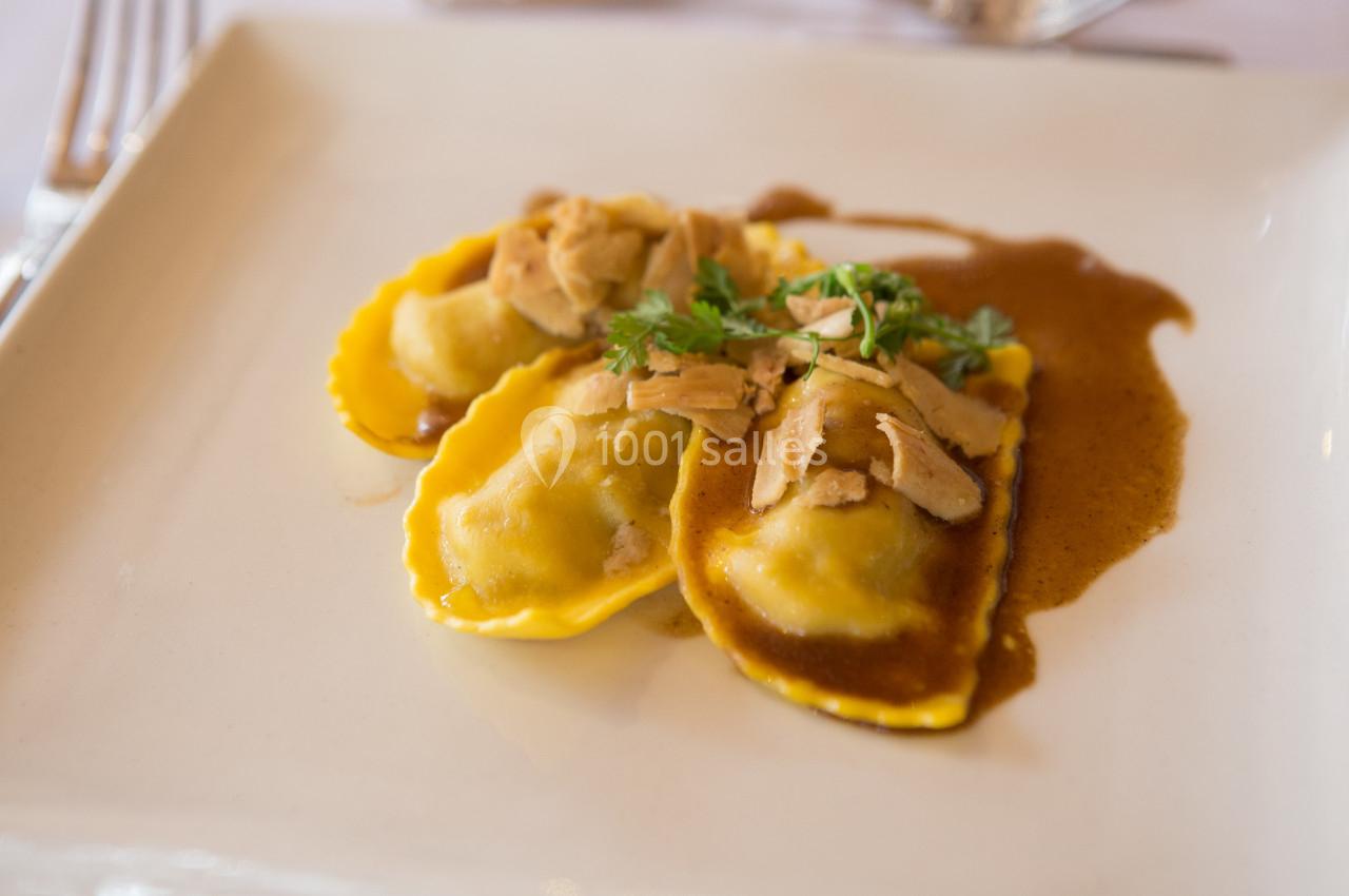 Assiette de raviolis garnis, nappés de sauce brune et garnis de morceaux de viande et de persil.