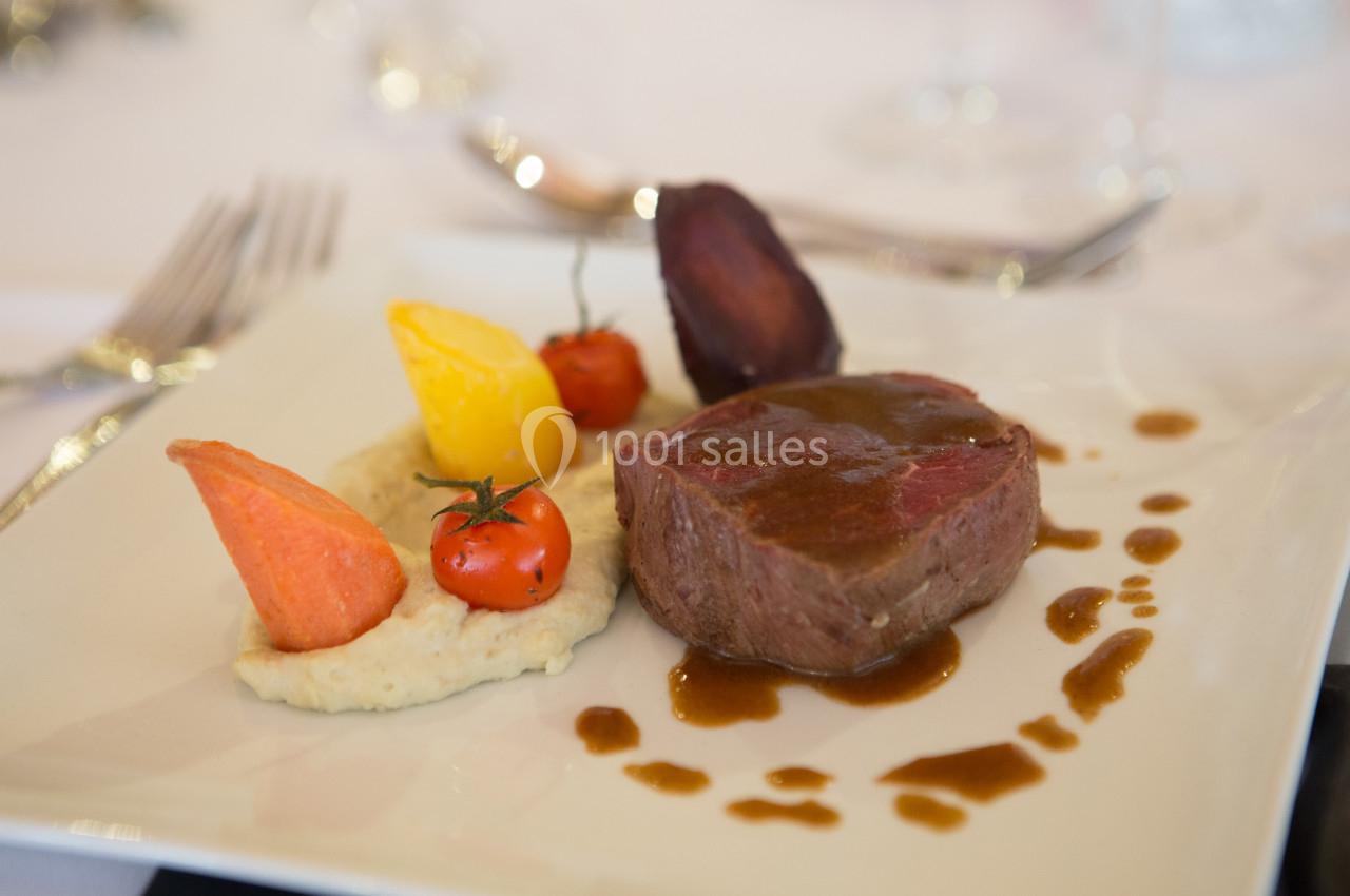 Assiette gastronomique avec un morceau de viande nappé de sauce, purée, légumes colorés et décoration soignée.