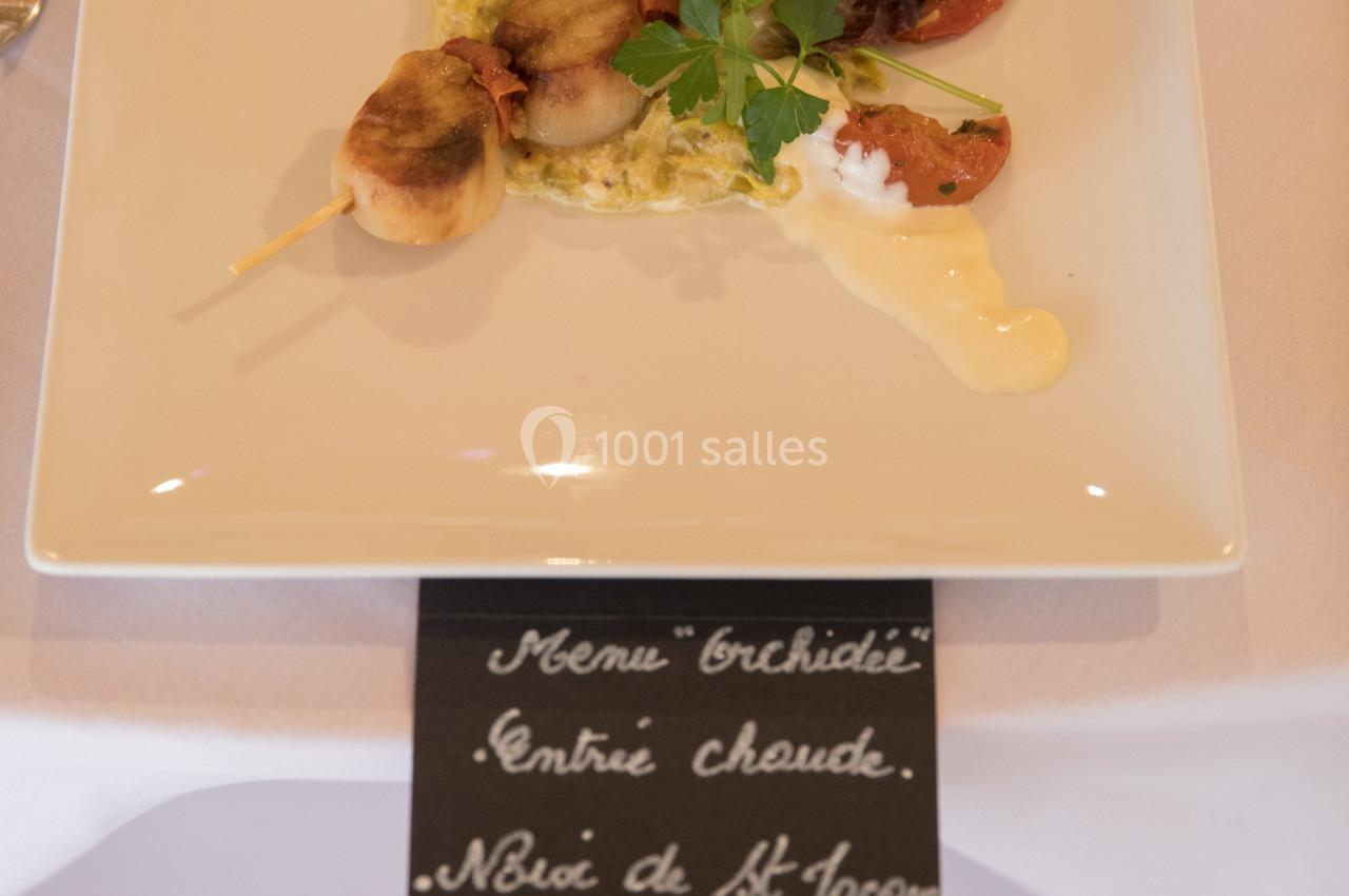 Brochette de noix de Saint-Jacques servie avec légumes, sauce crémeuse et décoration d'herbes sur une assiette carrée.