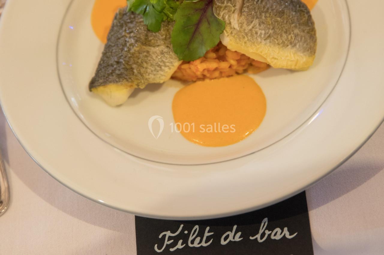 Assiette de filet de bar sur risotto aux poivrons rouges, décorée de verdure et sauce orangée.