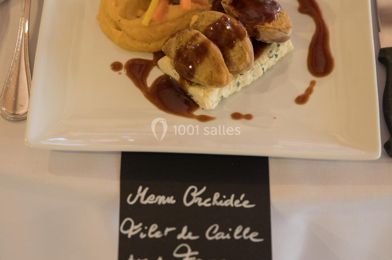 Assiette gastronomique avec filet de caille, purée, courgette farcie et sauce cassis, présentée sur une table dressée.