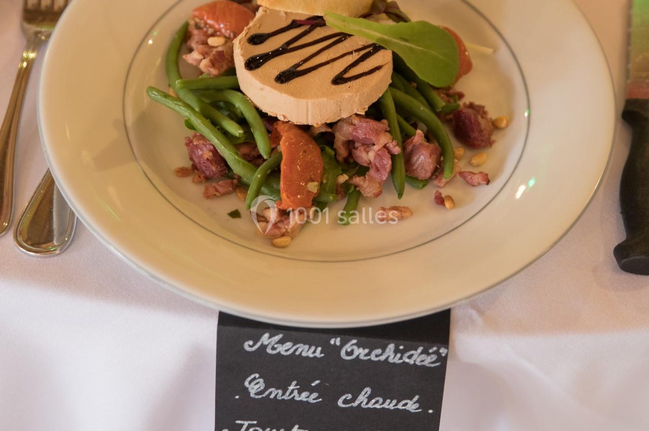 Assiette de salade composée avec haricots verts, magret de canard, noix, toast et sauce, présentée sur une table dressée.
