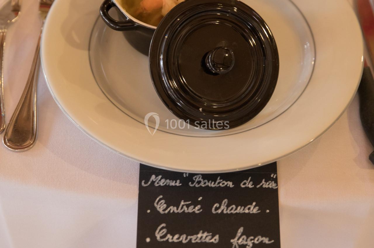 Mini cocotte contenant une entrée chaude aux crevettes, servie sur une table dressée avec couverts et ardoise descriptive.