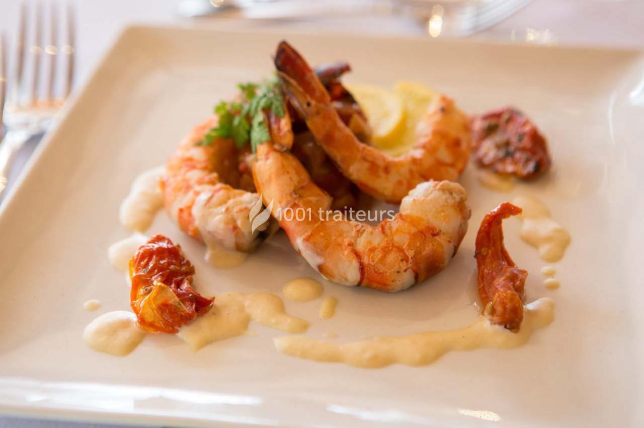 Assiette de crevettes grillées servies avec une sauce crémeuse, des tomates séchées et une tranche de citron.