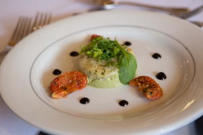 Assiette contenant une mousse verte garnie de persil, accompagnée de tomates rôties et de points de sauce balsamique.