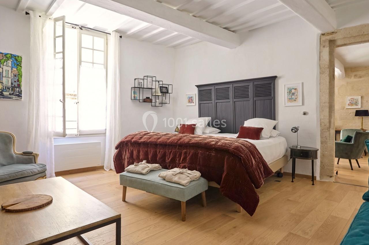 Chambre lumineuse avec lit double, couvre-lit rouge, fauteuils, table basse et décoration murale dans un intérieur…