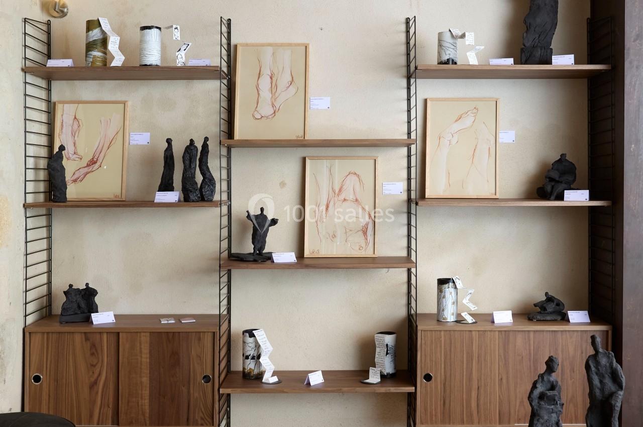 Étagères en bois et métal exposant des sculptures et dessins artistiques dans une pièce au mur beige et au plafond en…