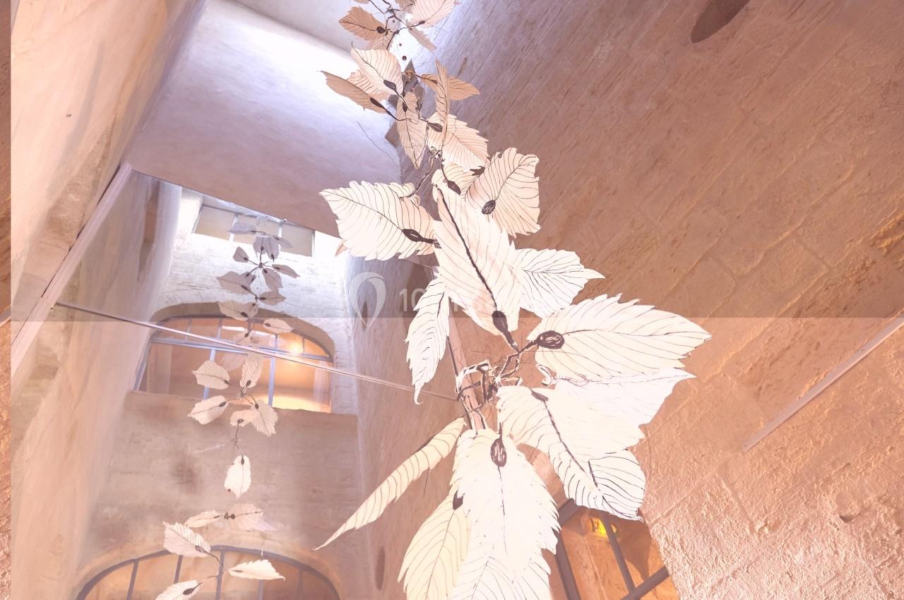 Installation artistique représentant des feuilles suspendues dans un espace architectural en pierre avec lumière naturelle.