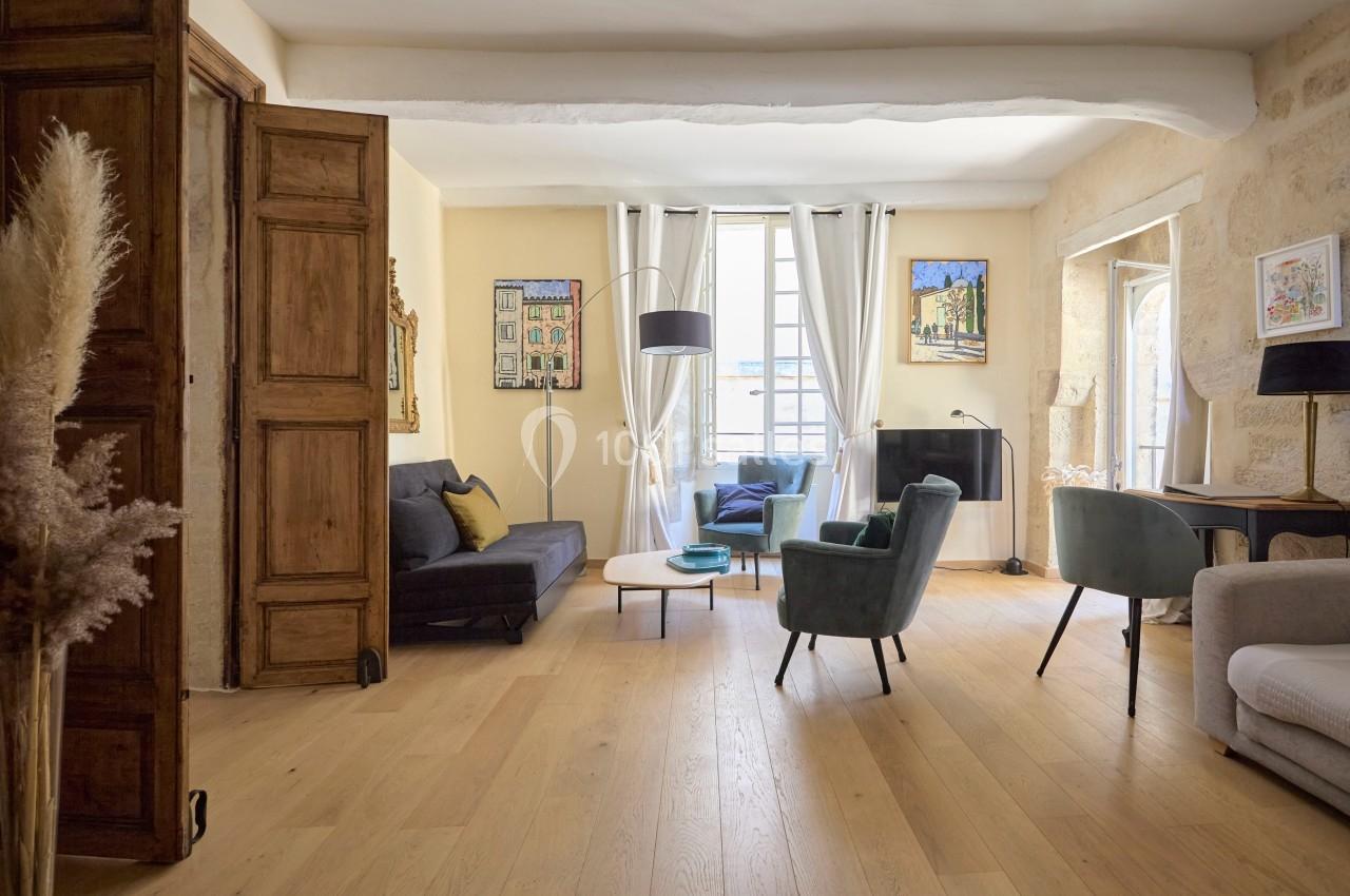 Salon lumineux avec parquet en bois clair, meubles modernes, murs en pierre et grande fenêtre laissant entrer la lumière.