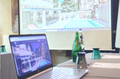 Salle de réunion avec tables disposées en U, chaises noires, bouteilles d'eau et écran de projection allumé.